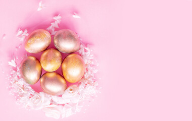 Obraz na płótnie Canvas Golden eggs in a flower nest on a pink background . Easter concept with space for text