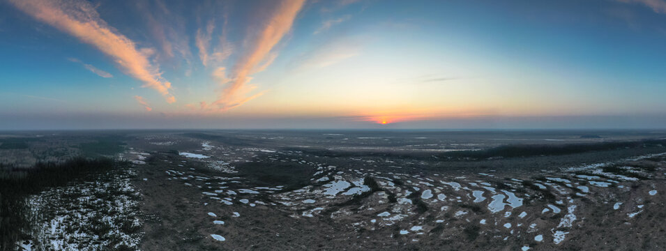 Aerial scenic panoramic view over early spring natural bog wetland with frozen pools and scenic sunrise in the sky