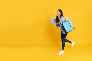 Side view portrait of happy young Asian woman running and holding baggage isolated on yellow...