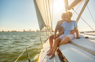 Relaxed senior couple sailing private yacht at sunset