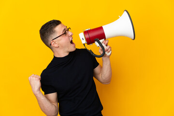 Young caucasian man isolated on yellow background shouting through a megaphone to announce...