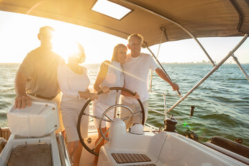 Seniors on vacation steering luxury yacht at sunset