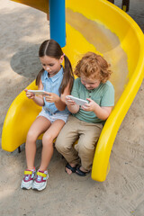 Fototapeta na wymiar high angle view of kids using smartphones while sitting on slide.