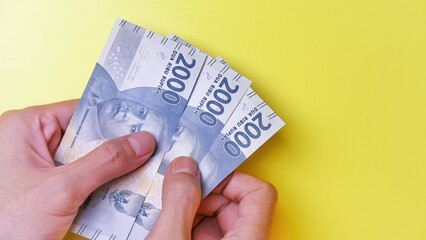 Indonesian Rupiah the official currency of Indonesia. Man's hand is making a payment. Business Saving Income Money Investment Economy and Finance Concept Uang 2000 2.000 Rupiah. Two thousand Rupiah.