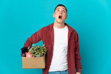 Young caucasian man making a move while picking up a box full of things isolated on blue background...