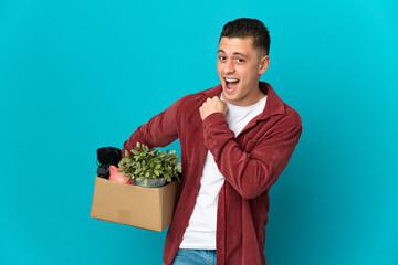 Young caucasian man making a move while picking up a box full of things isolated on blue background...