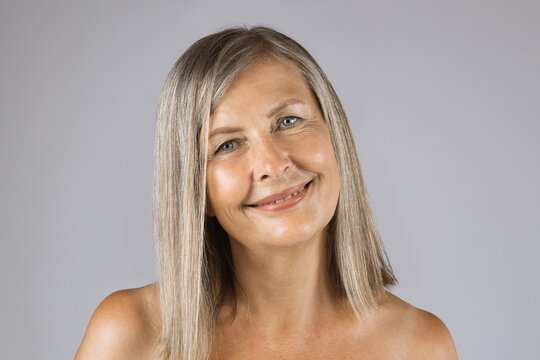 Portrait of caucasian mature woman with natural wrinkles on healthy skin posing over grey studio background. Beauty care and cosmetology concept.