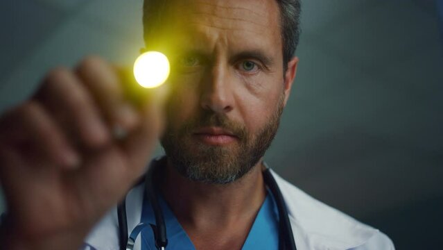 Doctor checking with flashlight test portrait. Serious male healthcare worker.