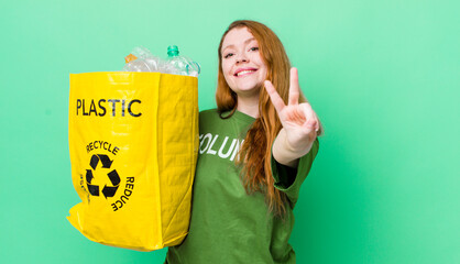 red head pretty woman smiling and looking happy, gesturing victory or peace. recycling concept