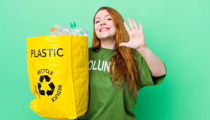 red head pretty woman smiling and looking friendly, showing number five. recycling concept