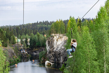 Young girl gliding  in  road trolley zipline over the lake  in the mountain park.