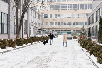Mature man holding ball near border collie and wife on street in winter.