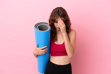 Young sport woman going to yoga classes while holding a mat isolated on pink background with tired...