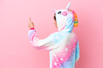 Young caucasian woman with unicorn pajamas isolated on pink background pointing back with the index...