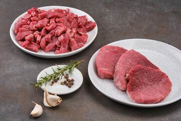 Fresh cut of beef in white plate with salt, pepper, garlic, rosemary. Raw steak beef meat fillet ready to cook. Selective focus