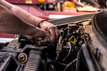 Mechanic with dirty hands works on car engine. Authentic shot of real auto mechanic working on motor.