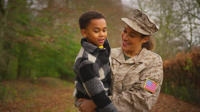 American female soldier in uniform coming home on leave carrying son outdoors - shot in slow motion