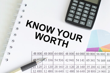 Know Your Worth inscription on a notepad on a table next to a calculator, pen, accounting reports and charts