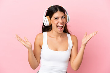 Naklejka premium Young caucasian woman isolated on pink background surprised and listening music