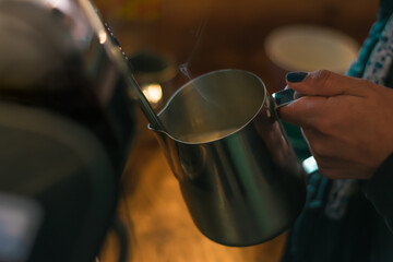 Unrecognizable woman's hand preparing textured milk on a professional espresso machine. Making a cappucino in a rustic coffee shop.