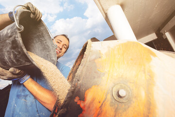 Close-up: a man pour out bucket of sand to cement mixer