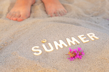 feet on the sand at the inscription summer from wooden letters