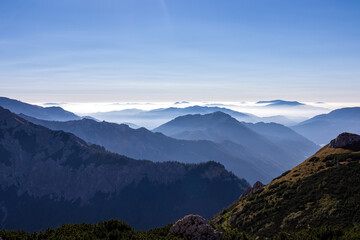 Obraz premium A panoramic view on the mountain peaks of the Hochschwab Region in Upper Styria, Austria. Cloudless weather on a sunny summer day in the Alps. Blue misty valley and soft hills. Concept freedom