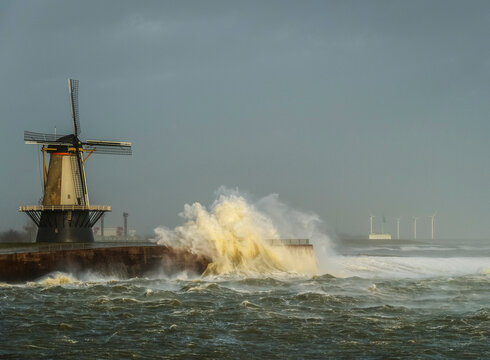 Netherlands, Vlissingen, Waves crashing against pier with windmill