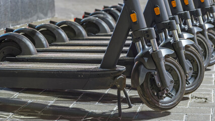 Electric scooters waiting at the curb ready to be rented and driven away. Several blue e-scooters stand in a row for rent.