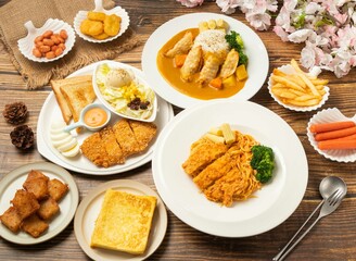 Assorted food French Toast, Fried small bean, chicken thighs, pasta spaghetti, hot dogs, Fried Dumpling, Curry Noodles Chicken Cutlet Platter, turnip cake, in dish side view on wooden table