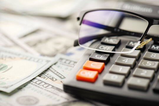 Close up photo of calculator spectacles and one hundred dollar banknotes