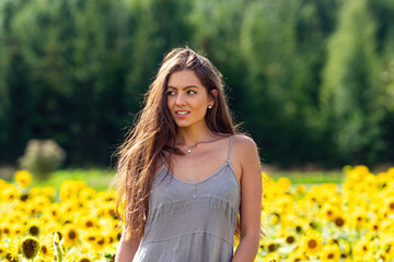 young woman with long hair in linean country style dress walks through a field of sunflowers
