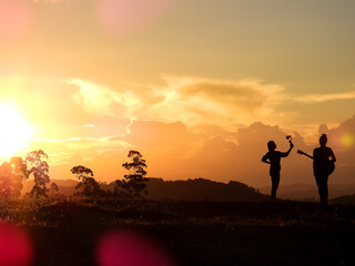 Orange sun setting in the mountains.  Man playing guitar silhouette and woman filming with gimbal and cell phone