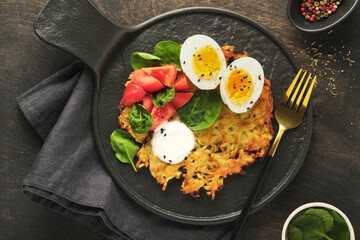 Potatoes latkes with sour cream, spinach salad, tomatoes and boiled eggs on dark wooden old table background. Homemade tasty potato pancakes. Delicious food for breakfast. Top view. - obrazy, fototapety, plakaty
