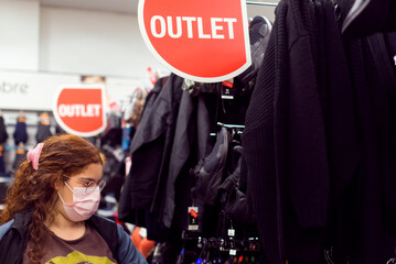 Real, young woman with protective mask shopping for clothes in an outlet store.