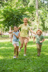 Fototapeta premium full length view of excited children with mother running in summer park.