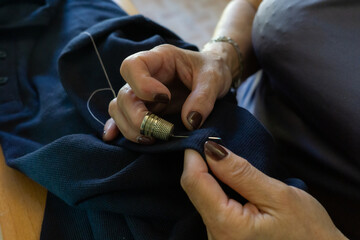 Unrecognizable woman sewing by hand with thread and thimble
