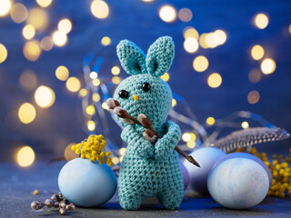 Easter knitted bunny toy and Easter colored eggs. Bokeh blue background.