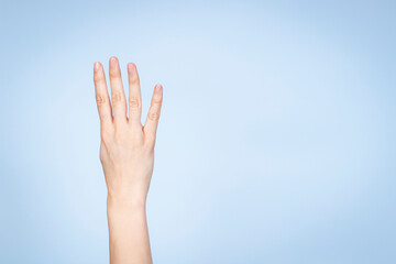 Female hand shows number four. Woman hand showing four fingers, pointing fingers up on light blue background