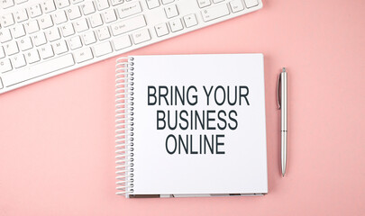 Pink office desk with keyboard and notebook with text BRING YOUR BUSINESS ONLINE ,business