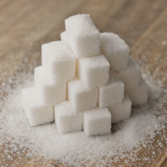 Lump sugar stacked in pyramid on wooden table. Sugar scattered on wooden surface.