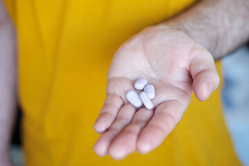 A male hand is holding four purple pills.