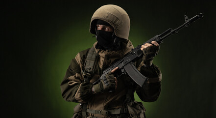 a Russian soldier in a helmet in military clothes with a Kalashnikov assault rifle on a dark...