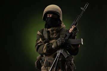 a Russian soldier in a helmet in military clothes with a Kalashnikov assault rifle on a dark...