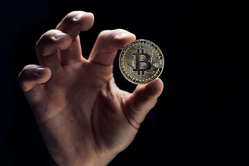Fototapeta na wymiar A businessman's hand holds a golden bitcoin and close-up of a hand with a coin. The concept of digital cryptocurrency, stock trading and the market.