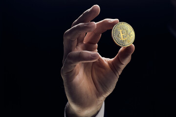 A businessman's hand holds a golden bitcoin and close-up of a hand with a coin. The concept of digital cryptocurrency, stock trading and the market.