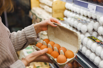 Woman chooses chicken eggs in a farm food store. Food consumption, Easter - obrazy, fototapety, plakaty