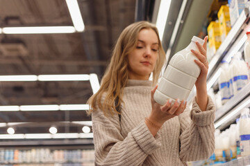 Grocery Shopping. Female read milk bottle In shop standing near shelf with dairy products