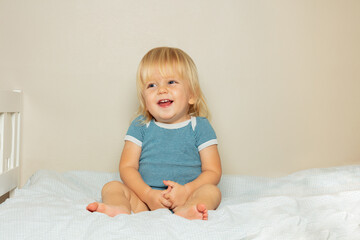 Fototapeta premium Laughing blond toddler boy sit on the bed in nursery