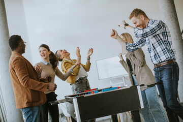 Young casual multiethnic business people playing table football and relaxing at office